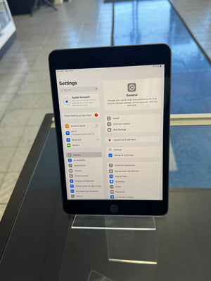 A tablet device with a black bezel displaying the Settings app, photographed indoors against a dark glass or acrylic surface with a blurred background.