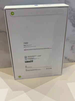 The back of a white Apple iPad box, showing product specifications and barcodes, set against a light marble-patterned background.