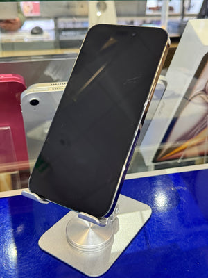 A black smartphone with a silver edge, resting on a silver metal stand on a glossy blue counter inside a retail store.