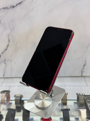 A red smartphone with a black screen is displayed on a silver metal stand in a retail setting, with a marble-patterned wall and watch displays visible in the background.