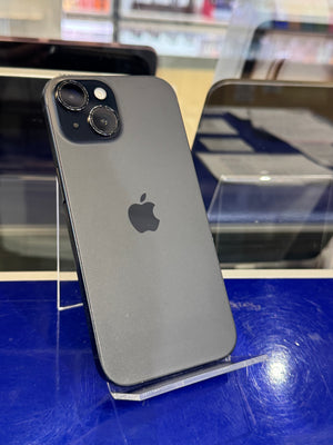 A dark gray Apple iPhone shown from the back, resting on a clear display stand on a blue surface.
