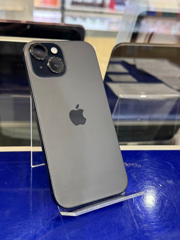 A dark gray Apple iPhone shown from the back, resting on a clear display stand on a blue surface.