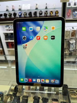 A tablet device with a black bezel and colorful home screen wallpaper, photographed in a retail display area with shelves of other gadgets in the blurred background.