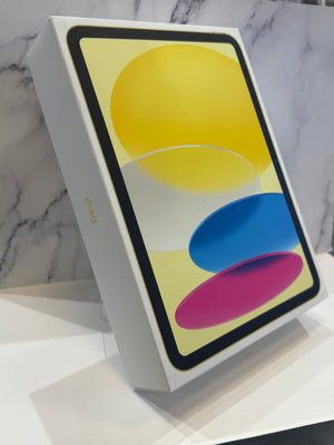 A white Apple iPad box shown at an angle on a white marble surface, with the front lid displaying a colorful abstract wallpaper and the word 'iPad' printed near the bottom.