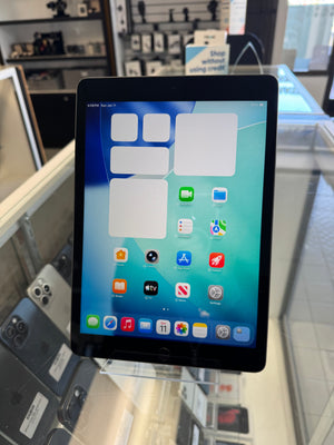A black tablet device displaying its home screen with various app icons, standing on a clear display stand inside what appears to be a retail store.