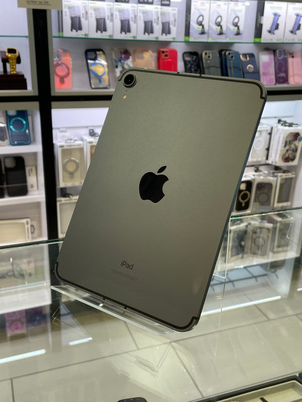 An Apple iPad with a dark gray metallic finish, shown from the back with the Apple logo visible, resting on a glass display counter in a retail store.