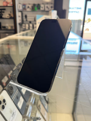 A black smartphone with a glossy screen, displayed on a clear acrylic stand inside a retail store. Other phones and store fixtures are visible in the blurred background.