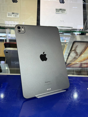 A silver Apple iPad shown from the back, resting on a blue display stand in a retail setting with Apple packaging visible in the background.