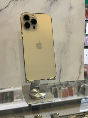A gold-colored Apple iPhone Pro shown from the back, resting on a silver metal display stand in front of a white marble-patterned wall.
