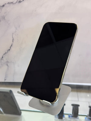 A black smartphone with a gold-toned edge, displayed upright on a metallic stand against a light marble-patterned background.
