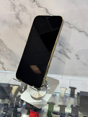 A gold-colored smartphone with a black screen stands vertically on a silver metal display stand. The background features a white marble patterned wall and a glass counter displaying other accessories.