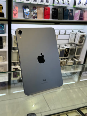 A silver Apple iPad shown from the back, standing on a glass display counter inside a retail store. The Apple logo and 'iPad' text are visible on the back of the device.