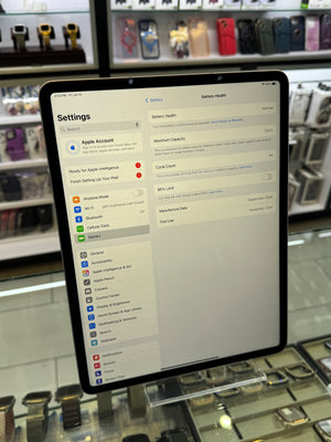 An iPad displaying the Settings app, showing battery information on the screen, photographed in a retail store environment with shelves of phone cases and watches in the background.