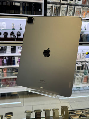 A gold Apple iPad Pro standing upright on a clear display stand inside a retail store, with shelves of electronics and accessories blurred in the background.