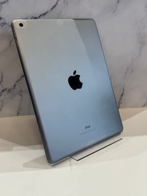 An Apple iPad with a metallic silver-gray back, standing on a clear acrylic display stand against a white marble-patterned wall.