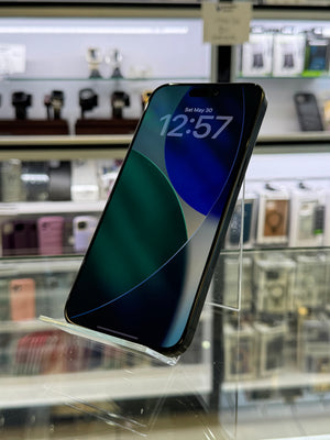 Smartphone with a reflective screen displaying the time '12:57' on a blurred background.
