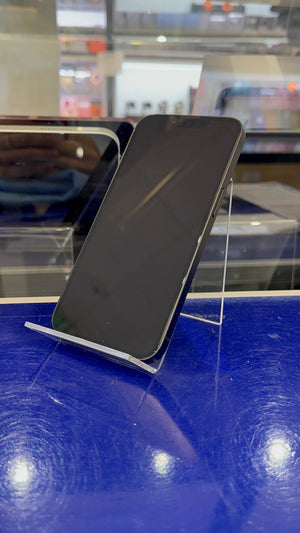 A black smartphone with a glossy screen, displayed on a clear acrylic stand on a blue reflective surface in a retail setting.