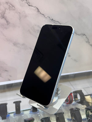 A silver smartphone with a black screen stands on a small metallic display stand in front of a marble-patterned wall. Other watch bands are visible in the blurred background.