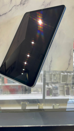 A black tablet with a silver edge, shown at an angle on a clear display stand against a white marble-patterned background.