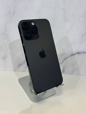 A black Apple iPhone 12 Pro shown from the back, resting on a clear acrylic display stand against a white marble-patterned background.