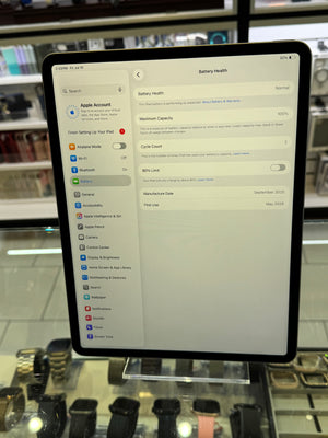 A tablet device shown in a retail display, with its screen turned on and displaying settings pages. The background contains glass cases with other electronic products.