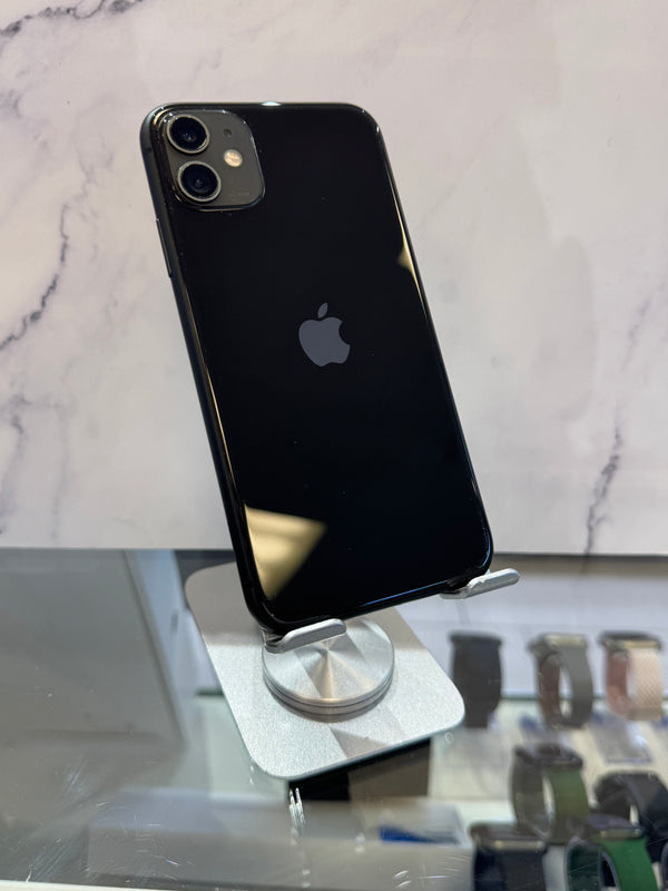 A black Apple iPhone 11 displayed on a silver stand, showing the back of the phone with its dual camera system and the Apple logo.