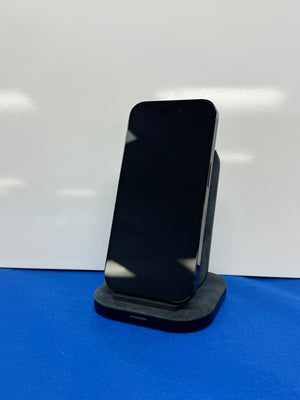 A black smartphone displayed upright on a dark charging dock or stand against a white backdrop with a blue surface below.