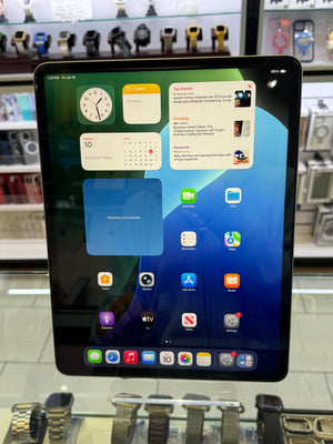 An iPad with a black bezel displaying the home screen, set on a glass display stand inside a retail store with watches in the background.