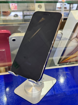 A black smartphone with a glossy screen resting on a silver display stand on a blue counter, with store fixtures visible in the background.