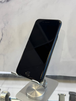 A black smartphone with a glossy screen resting on a silver metal stand against a white marble-patterned background.