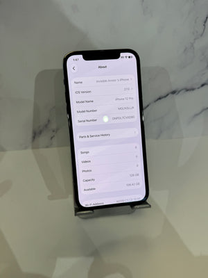 A black smartphone displayed upright on a small stand against a light marble-patterned background, with the screen turned on and showing an 'About' device details page.