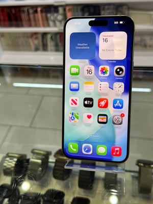 A black Apple iPhone with a lit home screen, displayed on a clear stand on a glass counter in a retail store.