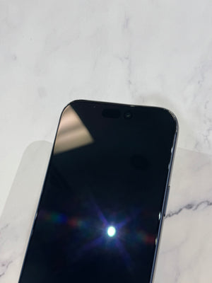 A close-up of a black smartphone showing the top portion of its glossy screen and front camera cutout, resting on a light marble surface.