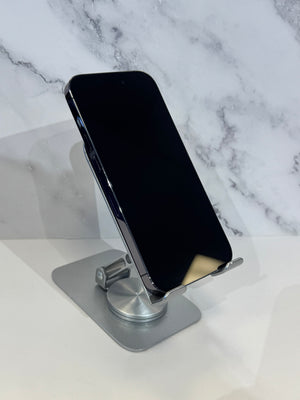 A black smartphone displayed at an angle on a silver metal stand against a white marble-patterned background.
