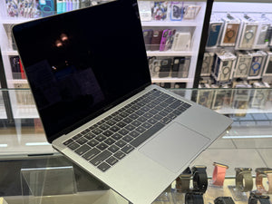 Open laptop on a glass surface with shelves of electronic products in the background