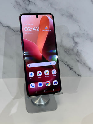 A black smartphone with a large front display stands upright on a silver metal stand against a white marble-patterned background.