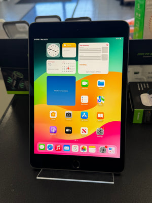 A black tablet device with a colorful home screen wallpaper, displayed upright on a clear acrylic stand on a dark tabletop.