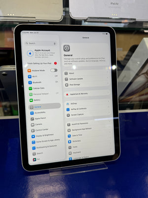 An iPad displaying the Apple Settings app on a blue display stand in a retail environment.
