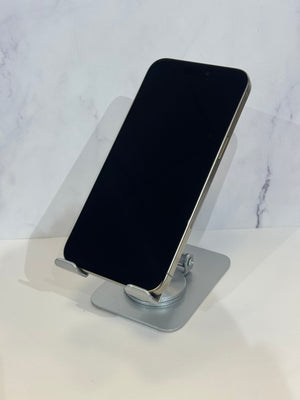 A silver metal phone stand holding a black smartphone, set against a light gray marble-patterned background.