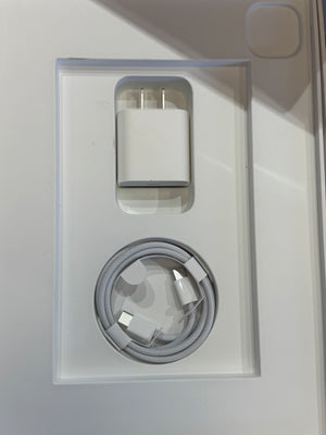 A white USB wall charger and a matching white charging cable displayed side-by-side inside a clear plastic tray on a white surface.