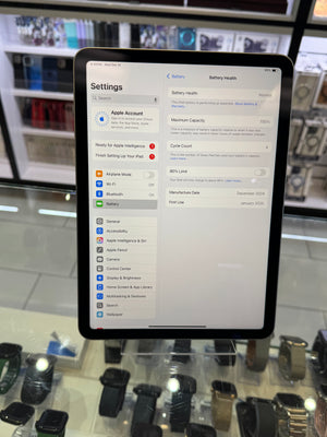 An iPad displaying the Settings app, specifically the Battery settings page, photographed in a retail store environment with display cases and other devices visible in the background.