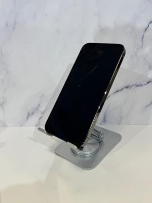 A black smartphone with a silver metallic edge resting on a clear acrylic stand over a silver base, set against a white marble-patterned background.