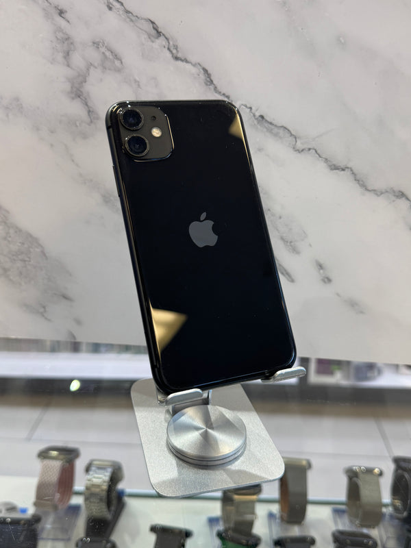 A black Apple iPhone with a glossy finish, resting on a silver magnetic display stand on a white marble surface.