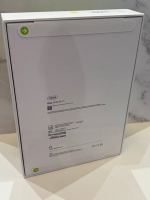 The back of a white Apple iPad box, showing product specifications, barcodes, and recycling symbols, photographed on a light marble surface.