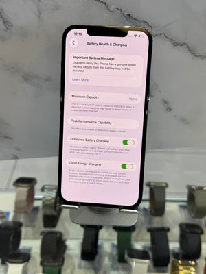 A smartphone displaying the iOS Battery Health & Charging settings screen, standing on a display stand in front of a marble-patterned background with watch faces blurred below.