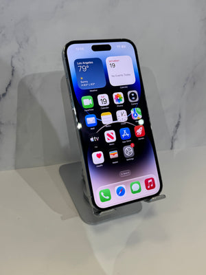 A black Apple iPhone with a silver bumper stands on a clear acrylic display stand against a light gray marble-patterned background.
