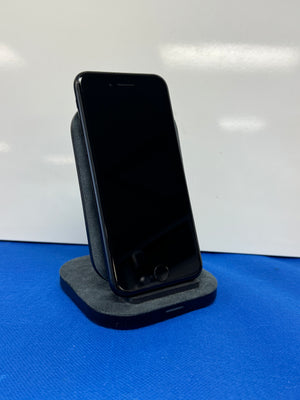 A black smartphone displayed upright on a dark gray fabric phone stand against a white background with a blue surface below.
