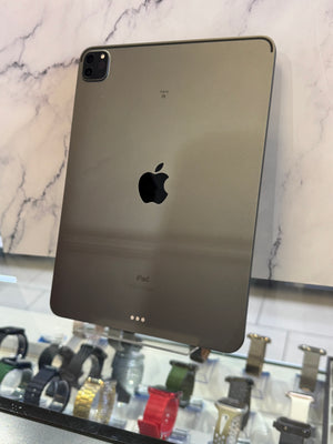 A dark gray Apple iPad shown from the back, resting on a white marble-patterned surface with a glass display case containing watches visible in the background.
