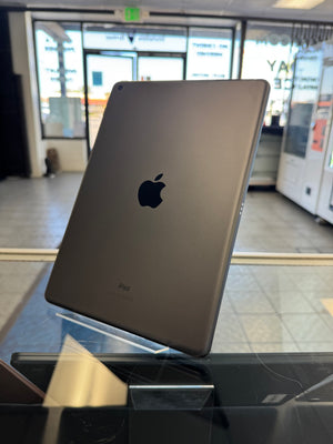 A dark gray Apple iPad Pro standing upright on a glass display stand inside a retail store.