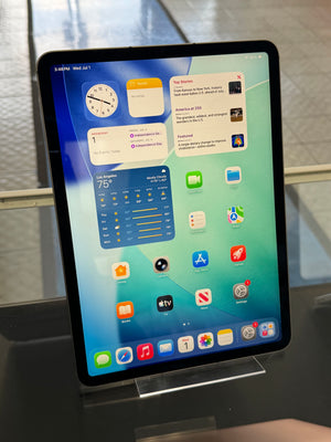 iPad with display on showing various apps on the home screen standing in an acrylic stand on a store shelf